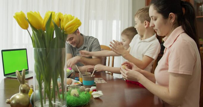 Happy family painting Easter eggs in kitchen