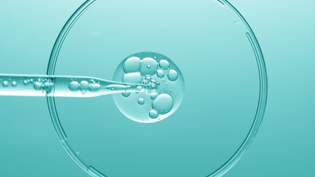 Close up view macro shot of gel with different sized bubbles comes out from lab dropper into petri dish on cyan background | Abstract face care gel with hyaluronic acid mixing concept