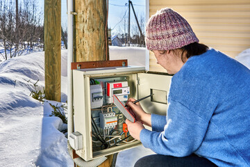 Taking electric meter readings by woman outside in village in winter.