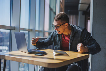 Portrait of a man, IT professional, working remotely with a modern laptop, sitting at a table and smiling at the camera during a break, a happy human programmer in vision correction glasses