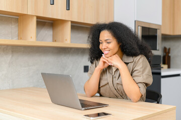Smiling business woman using laptop for remote work from home. Confident lady checking emails, conducting business correspondence while sitting at the table, looks at the screen