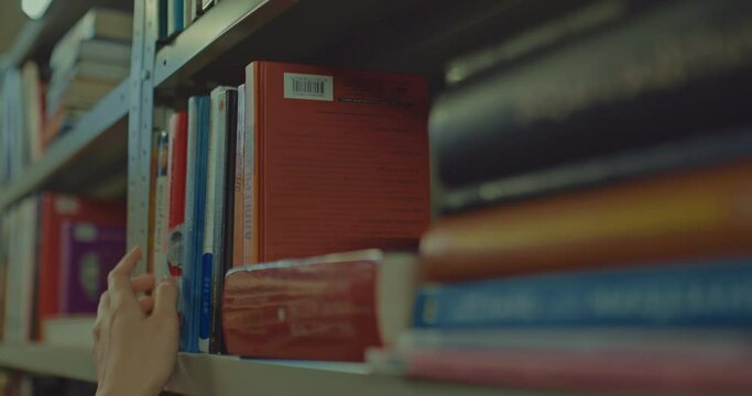 Close-up, the books are on the shelves of the rack. Hands of a man and a woman touch books, choose interesting literature. Reading room of the library, book lovers. 4k, ProRes