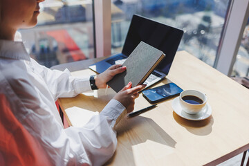 Notepad for entries in female hands on the background of a laptop close-up, a cup of coffee on a wooden table. Businessman's desk. Working process. selective focus