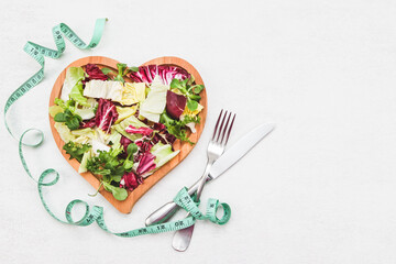 Lettuce leaves in a heart-shaped wooden plate, a measuring tape and a knife with a fork on a cement.