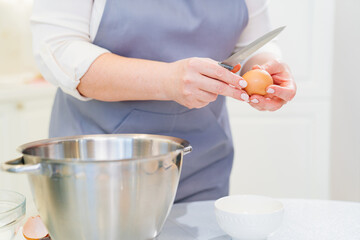 A woman breaks an egg with a knife to prepare cream or dough in a mixer bowl.