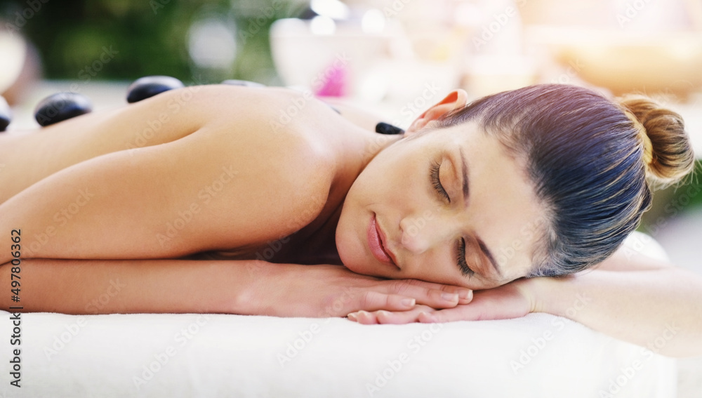 Wall mural Cant help but drift away in such a magical state. Shot of a young woman getting a hot stone massage at a spa.