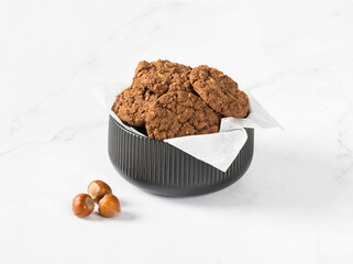 Chocolate oatmeal cookies with hazelnuts in a serving bowl. White background
