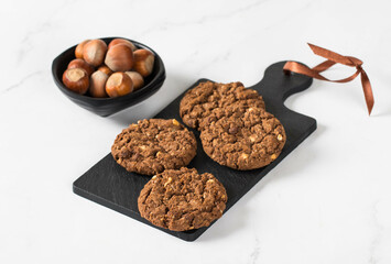 Chocolate oatmeal cookies with hazelnuts on a serving board. White background