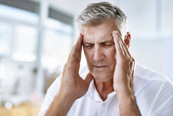 Trying to be productive but this headache isnt helping. Shot of a mature businessman suffering with a headache at work.