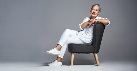 Relax, youve earned it. Studio shot of a senior woman sitting on a chair against a grey background.