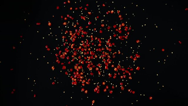 Whole raw fresh red chili peppers and finely chopped scattered over a black background, top close up shot.