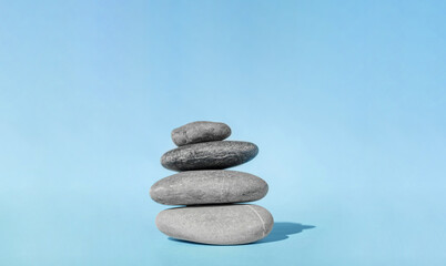 Fototapeta na wymiar Balanced pebble stones for spa treatments on blue background. The balancing cairn - symbol of harmony, tranquility and relaxation, concept of meditation. Stack of spa hot stones.