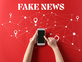 Child's hands with modern mobile phone and text FAKE NEWS on red background, top view