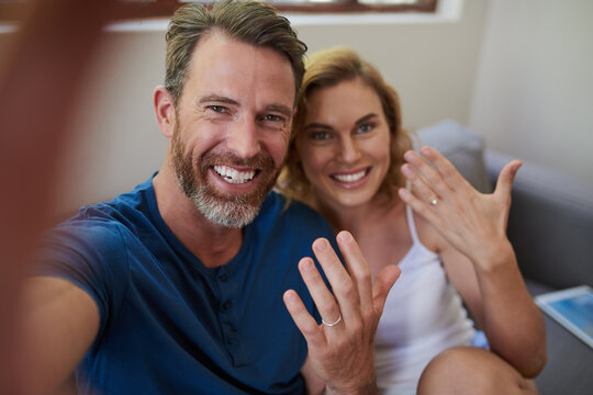 Look who just got married. Shot of a happy middle aged couple taking a selfie and showing off their wedding rings at home.