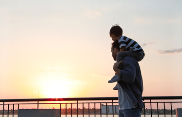 Fototapeta premium Father carrying his little son near river at sunset