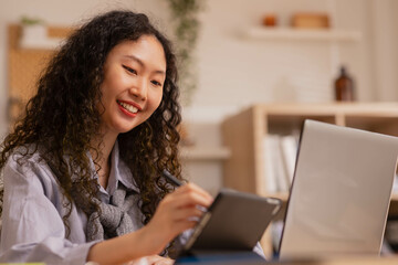 In the morning, an Asian designer works on a tablet with a stylus, sketching and writing designs.