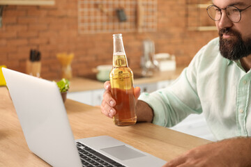 Man with laptop drinking beer in kitchen