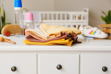 Stack of baby clothes with toys and bottles on table in room, closeup