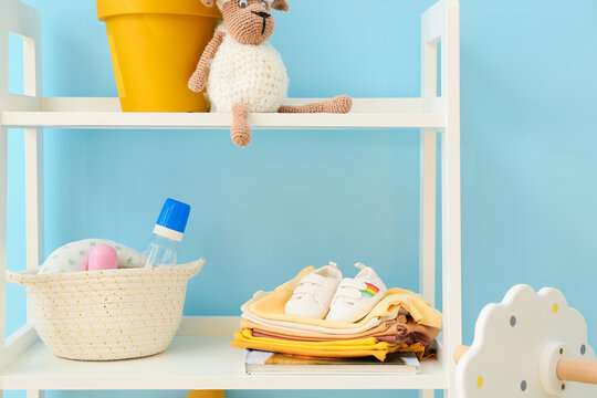 Shelving Unit With Baby Clothes, Bottles And Toys Near Blue Wall