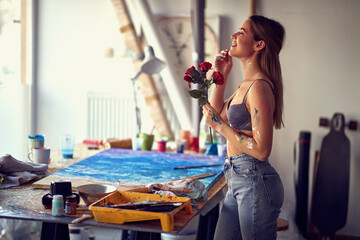 A thoughtful sexy and attractive female artist in her studio is in ecstasy while holding roses she got. Art, painting, studio