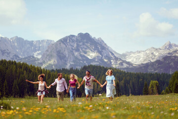 Fototapeta na wymiar Young friends in casual clothing running through meadow holding hands, enjoying time in nature, summertime. Fun, togetherness, lifestyle, nature concept.