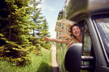 Blonde woman on the window of an rv with hands out smiling enjoying ride. Vacation time. Transport, roadtrip, nature concept. - 497816995