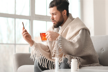 Ill man with sore throat drinking hot tea while video chatting with doctor at home