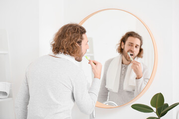 Handsome young man brushing teeth near mirror in bathroom