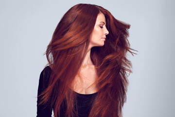 Lovely luscious locks. Studio shot of a young woman with beautiful red hair posing against a gray...