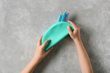 Child holding pencil case with color pencils on light background