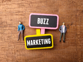Wooden board and miniature people with text BUZZ MARKETING on a wooden background.