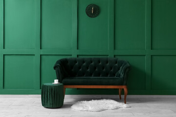 Fototapeta na wymiar Comfortable sofa and pouf near green wall
