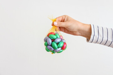 Woman holding mesh bag with chocolate Easter eggs on light background, closeup