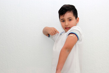 8-year-old Hispanic boy wearing a school uniform shirt happily shows his recently vaccinated arm...