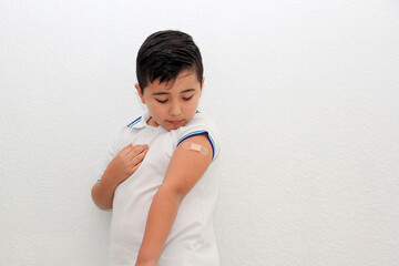 8-year-old Hispanic boy wearing a school uniform shirt happily shows his recently vaccinated arm...