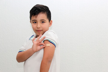 8-year-old Hispanic boy wearing a school uniform shirt happily shows his recently vaccinated arm...