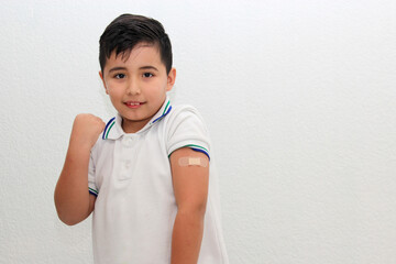 8-year-old Hispanic boy wearing a school uniform shirt happily shows his recently vaccinated arm against Covid-19 in the new normality due to the Coronavirus pandemic
