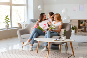 Young woman, her little daughter and mother with flowers and greeting card on International Women's Day at home