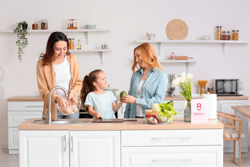 Happy young woman, her little daughter and mother cooking together in kitchen at home....
