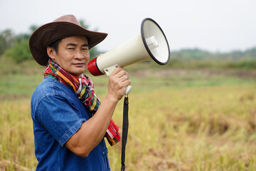 Asian farmer holds a megaphone at agricultural field. Concept : communication , announcement. Protest. Protester. Announce something to the world. Bullhorn public address megaphone.           