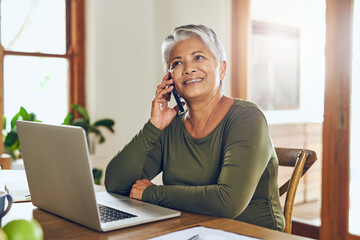 Her broker just called with some more good news. Shot of a mature woman talking on a cellphone while working on a laptop at home.