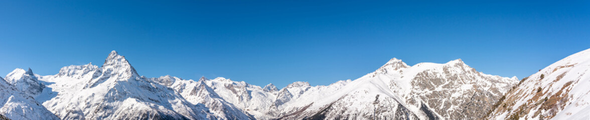 Panoramic view of winter snowy mountains in Caucasus region in Russia with blue sky
