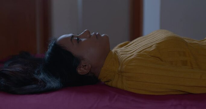 apathetic depressed indian woman lying on the bed looking serious at camera