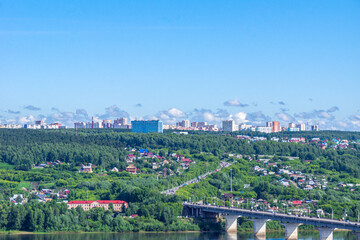 Village houses on shore and multi-storey residential buildings behind forest , in foreground road bridge across River