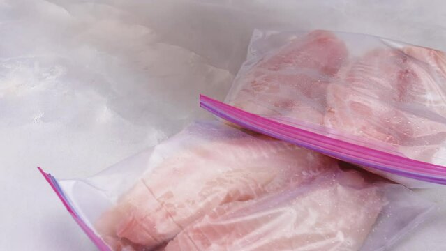 Fresh raw fish fillet in zip lock bags. Tilapia fillet on light marble background, close up view 