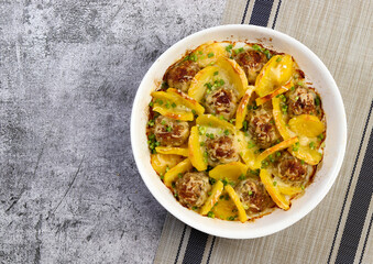 Potato with meatballs in a white baking dish on a dark grey background. Top view, flat lay