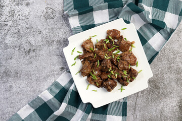 Pan fried chicken liver with herbs on a white square  plate on a dark background. Top view, flat lay
