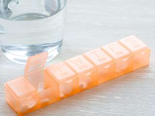 Orange pill box and a glass of water. Prescription drugs in seven day pill case. Patient organizes...