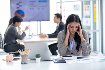 Tired asian business woman with headache at office, feeling sick at work with laptop and book on her desk.