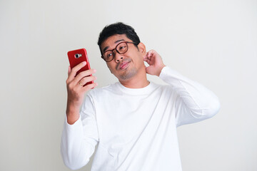 Adult Asian man showing so lazy expression while checking his mobile phone after wake up in the morning - obrazy, fototapety, plakaty